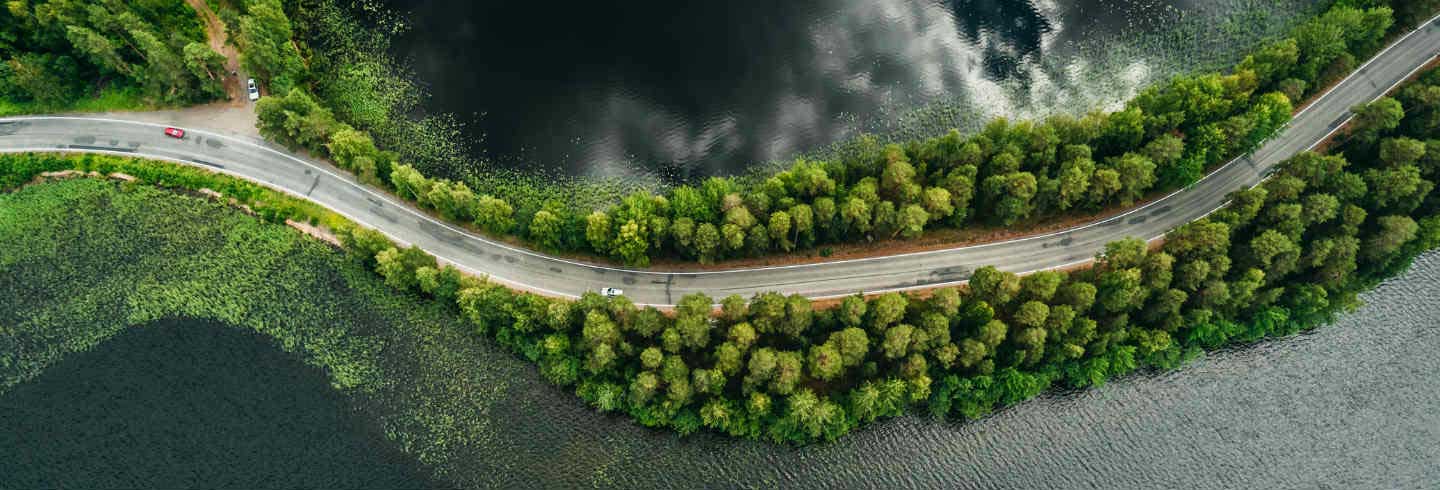Un coche viaja a través de una carretera entre bosque y lago 