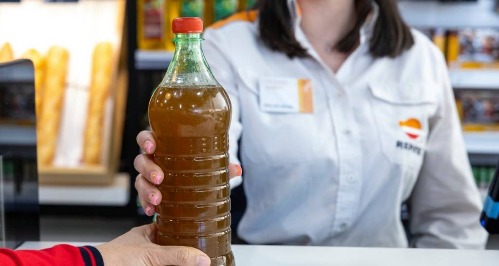 Una persona reciclando una botella de aceite de cocina usado