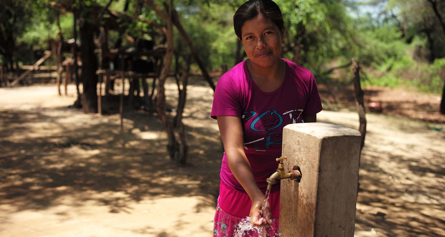 Mujer boliviana se moja la mano en una fuente 